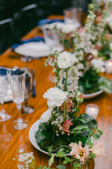 Elegant floral arrangements adorn a wooden dining table set for a special event in an intimate venue on a calm evening
