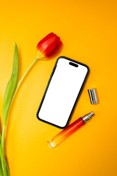 Mock-up phone with white blank screen on the yellow background with red tulips and red bottle of parfums