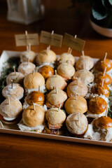Variety of mini sandwiches arranged on a wooden table at an outdoor gathering during daytime
