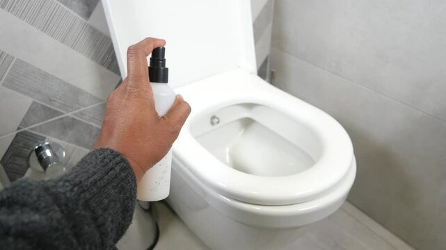 A person sprays a cleaner in the toilet bowl
