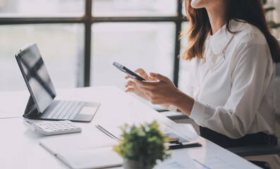 Young asian woman talking on mobile phone while taking notes and working with laptop computer at home. Business, home office and technology concept.