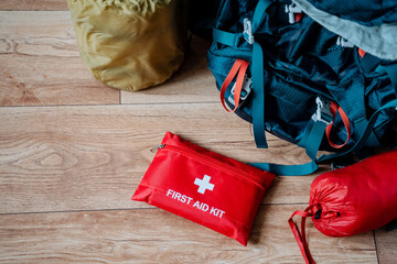 A wellequipped first aid kit is sitting on a polished wooden floor next to an outdoor backpack, which is likely packed with essential items for a day of adventuring in nature