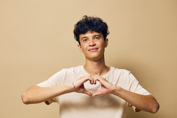 young man making heart shape with hands, warm background, smiling expression, positive emotions,...