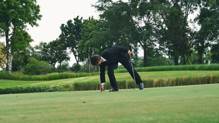 Businessman playing Golf ball practice hit swing on tee in golf club outdoor green field with recreation sport training course. Business men with black Suit driving golf Hobbies
