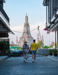 A couple walks hand in hand down a quaint alley in Bangkok, Thailand, drawn toward the majestic Wat...