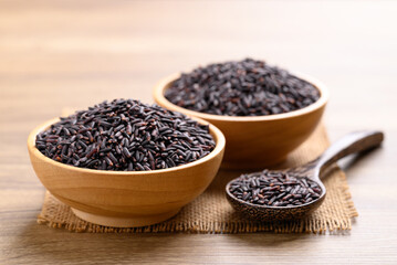 Organic rice berry or purple rice in wooden bowl with spoon on wooden background, Thai rice