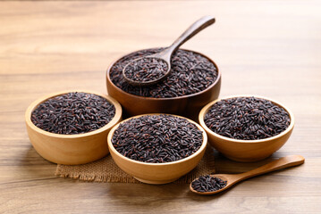 Organic rice berry or purple rice in wooden bowl with spoon on wooden background, Thai rice