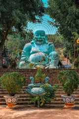 Smiling teal buddha statue surrounded by vegetation