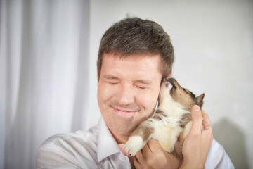 Man smiles while cuddling a small puppy in a bright room, capturing a joyful moment of...