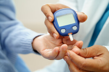 Asian doctor using digital glucose meter for check sample blood sugar level to treatment diabetes.