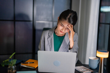 Alone Working Late at Night. Asian business woman at workplace in office late night work at a desk in a dark office working on a laptop late in the evening..
