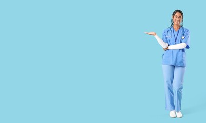 Young African-American female doctor showing something on light blue background with space for text