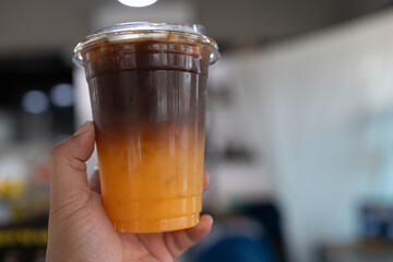 Iced americano black coffee and layer of orange juice in hand