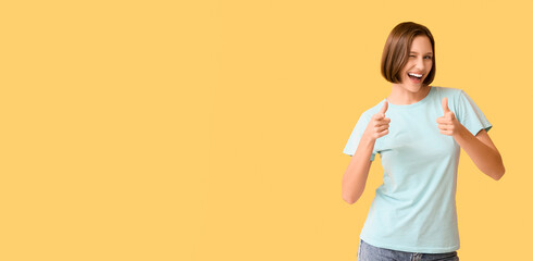Young woman in blank t-shirt pointing at viewer on yellow background