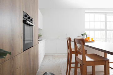 Interior of light kitchen with built-in oven, island and chairs