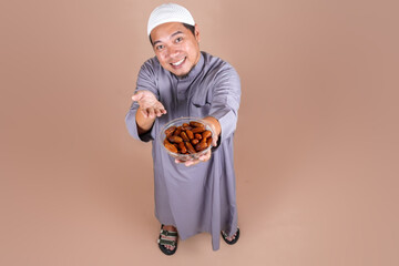 High Angle of Asian Muslim Man Showing Dates Fruit on Bowl Isolated on Beige Background