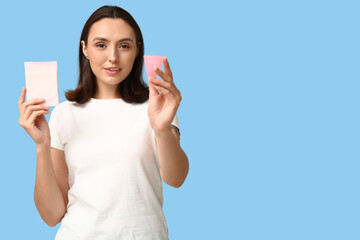 Beautiful young woman with menstrual cup and pad on blue background