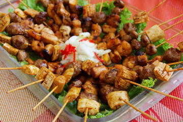 Satay containing squid, meatballs and shrimp on lettuce leaves, garnished with sliced ​​cucumber and sliced ​​red chili peppers