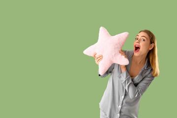 Shocked young woman with soft pillow in shape of star on green background