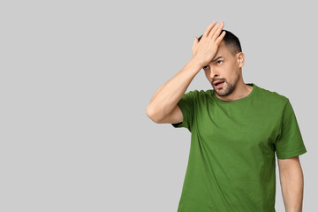 Handsome worried young man covering face with hand on grey background