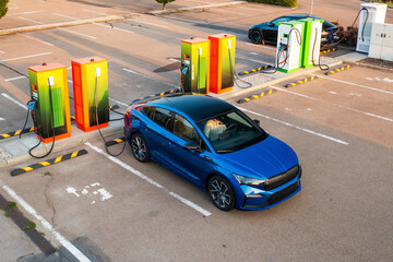 Modern vehicle receives electricity at public charging point. Parking lot equipped with plugs and...