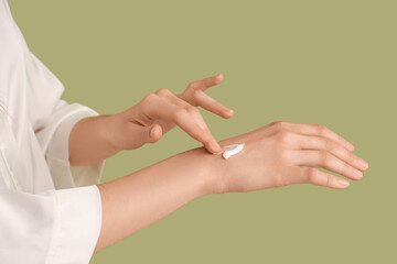 Woman applying cream onto hands on green background, closeup