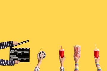 Many hands with movie clapper, bucket of popcorn and drinks on yellow background