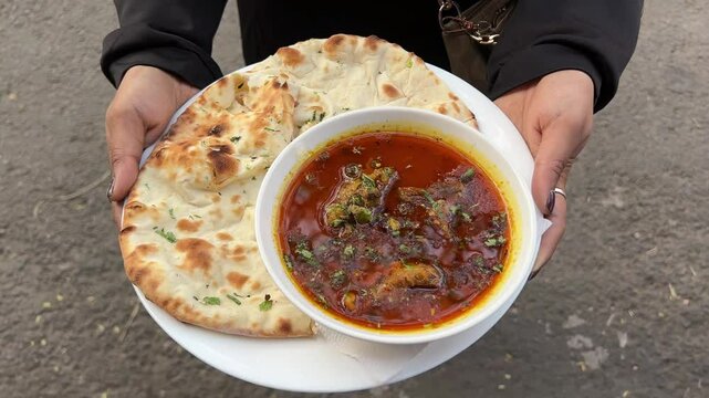 Footage of naan with dhaniya paratha with mutton nihari on diposable plate.