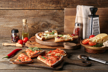 Boards with tasty pizzas, kitchen utensils and ingredients on wooden background