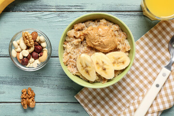 Bowl with tasty oatmeal, banana, peanut butter and nuts on wooden background