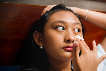 Southeast Asian teenage girl cleaning and removing makeup from her face using cotton. Routine skincare for beauty tips concept.