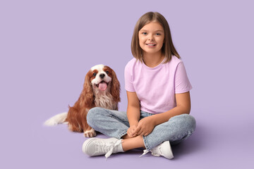 Cute little girl with King Charles spaniel dog sitting on lilac background