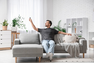 Fototapeta premium Handsome young man switching on air conditioner at home