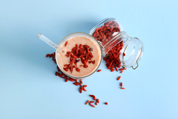 Glass of fresh goji smoothie and jar with berries on blue background