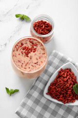 Glass of fresh goji smoothie and bowl with berries and mint on white background