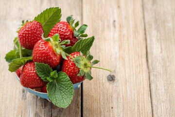 A bowl of strawberries and mint leaves on a wooden table