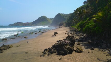 Aerial drone view of coastline with hills and trees, as well as view of coral cliffs and sea with waves from the ocean in Pecaron Beach Kebumen Central Java Indonesia