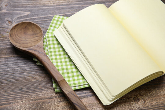 Blank recipe book, spoon and napkin on wooden background, closeup