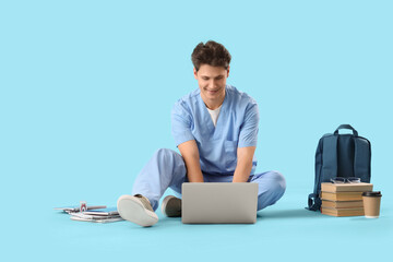 Male medical intern studying with laptop on blue background