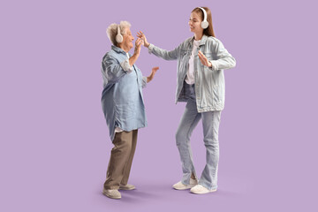 Naklejka premium Happy senior woman and her granddaughter in headphones dancing on purple background