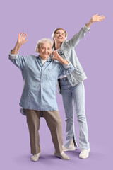 Happy senior woman and her granddaughter in headphones dancing on purple background