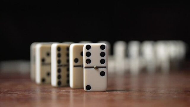 A finger pushes a spiral of white dominos, triggering a slow-motion chain reaction and domino effect in motion