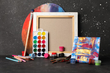 Artist brushes, paints, canvas and painting on black grunge background