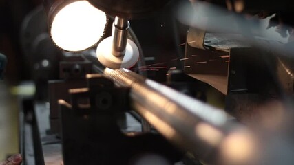 A spinning grinder machine is sharpening the ridged edges on a broach tool inside of a manufacturing company.
