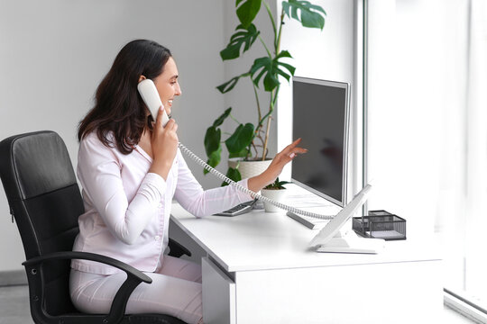 Young businesswoman talking by phone at table in office. National Wear Your Pajamas to Work Day