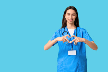 Young female doctor making heart gesture on blue background