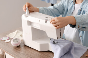 Young female tailor using sewing machine near table in atelier, closeup