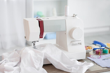 Modern sewing machine with white shirt and tailor's supplies on table in atelier