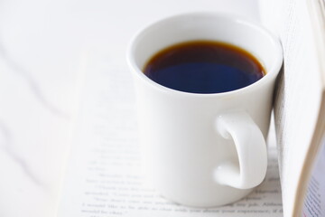 ページを開いたペーパーバック（洋書）とコーヒーの入ったコーヒーカップで、コーヒーを飲みながら読書を楽しんでいるイメージ
