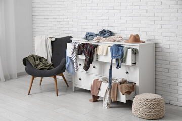 Interior of messy room with armchair, commode and different scattered clothes